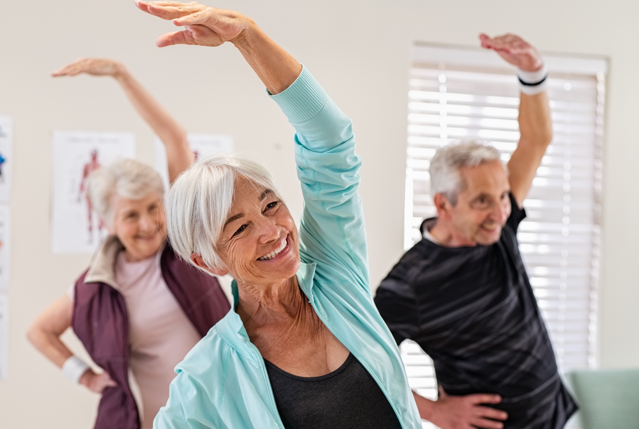 Group of seniors doing stretching exercise together at retirement centre. Elderly men and old women exercising at nursing home during daily fitness. Retired couples exercising at care facility.