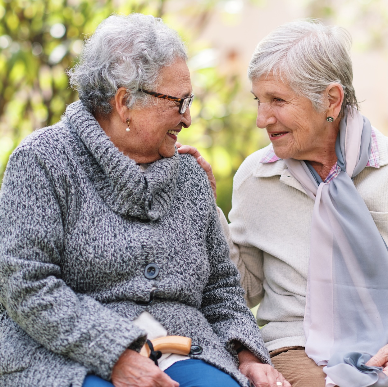 Two elderly women sitting on bench in park smiling happy life long friends enjoying retirement